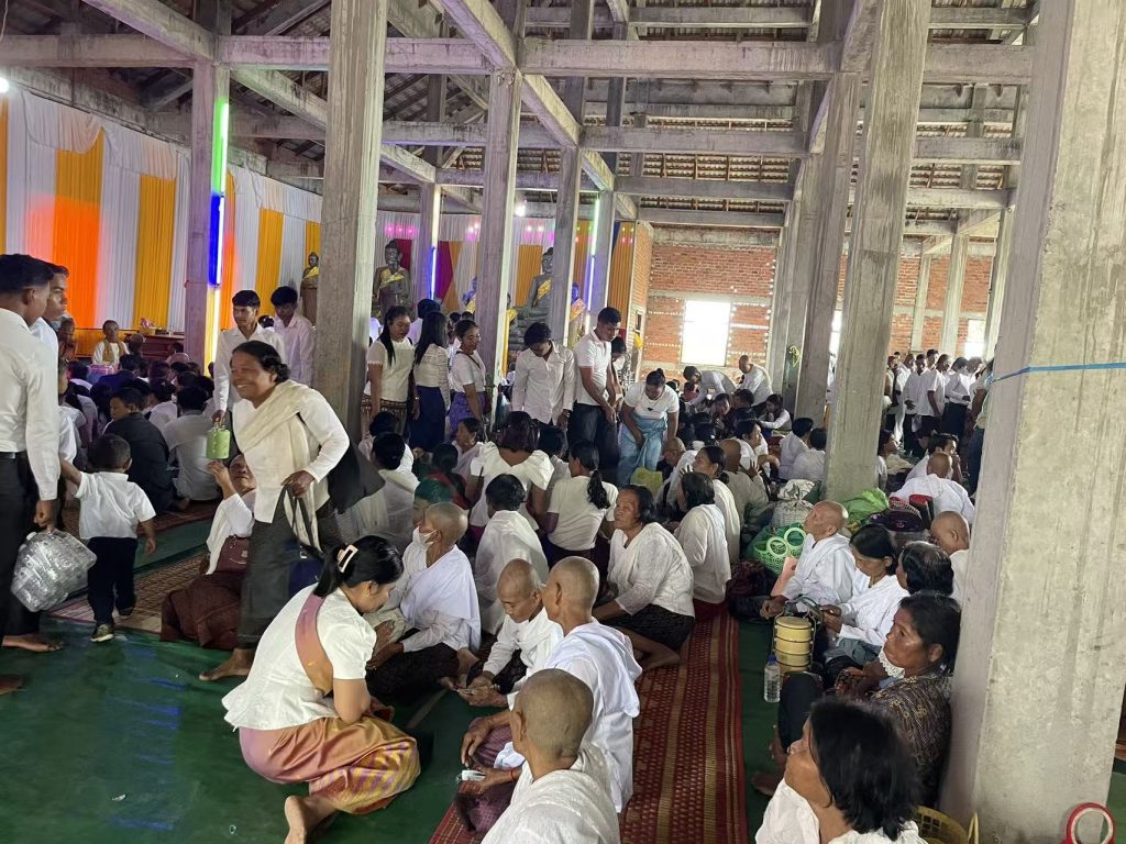 Cambodian families gathered inside a temple during Pchum Ben Festival, dressed in traditional white clothing to make offerings and pray for ancestors.